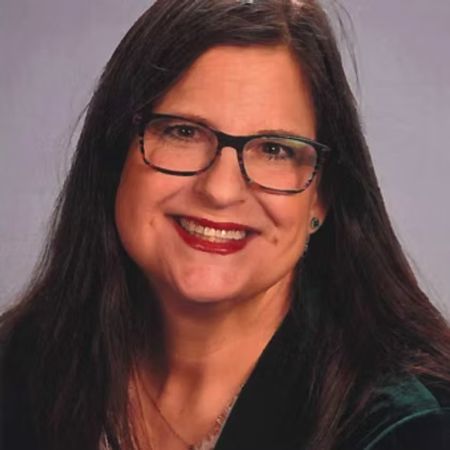 Photo of a smiling woman with long brown hair against a tree background